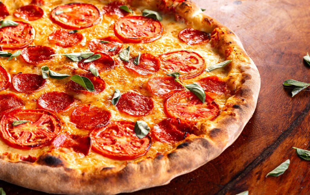 Mouthwatering pizza topped with fresh tomatoes, pepperoni, and basil on a rustic table.